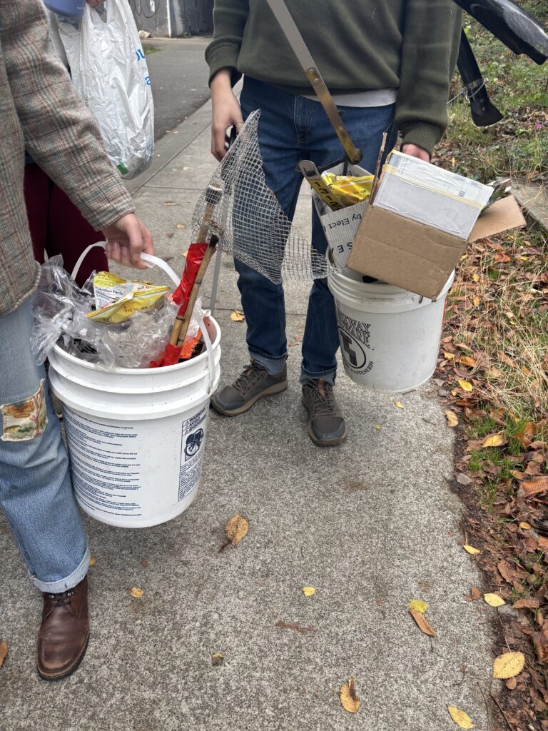 People carry buckets full of trash. The lighting and leaves on the ground say it's fall.